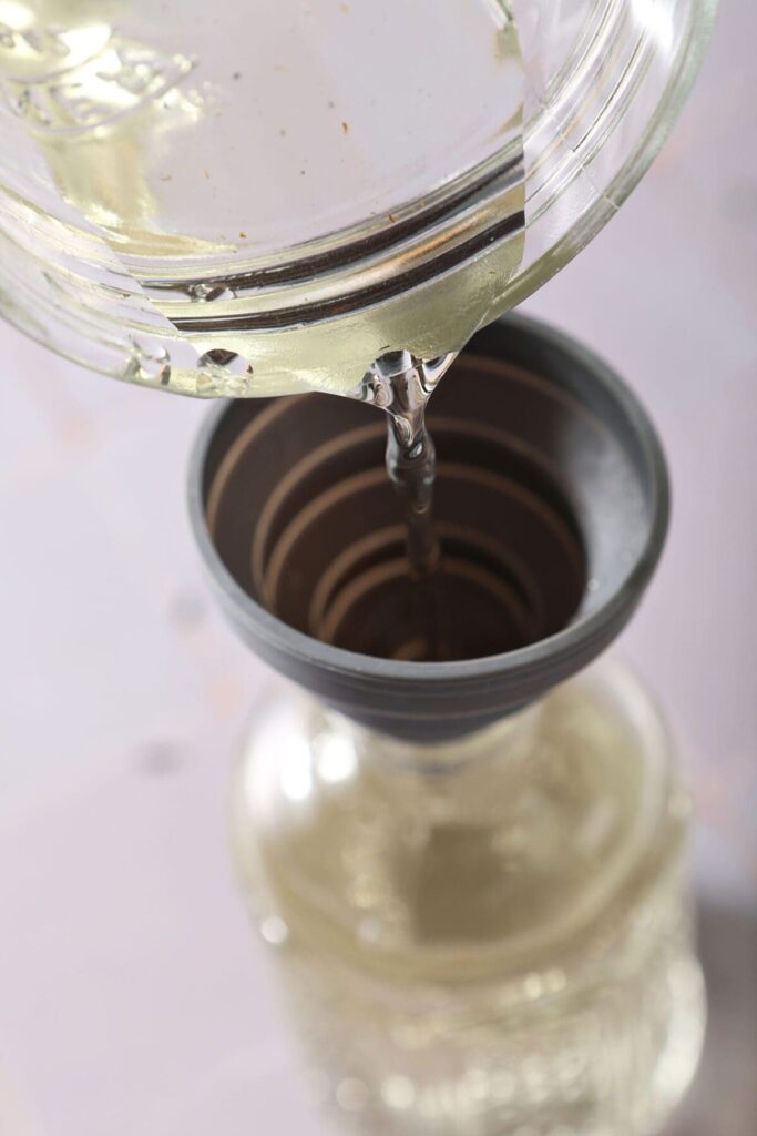 Lavender simple syrup pours into a funnel to go into a jar