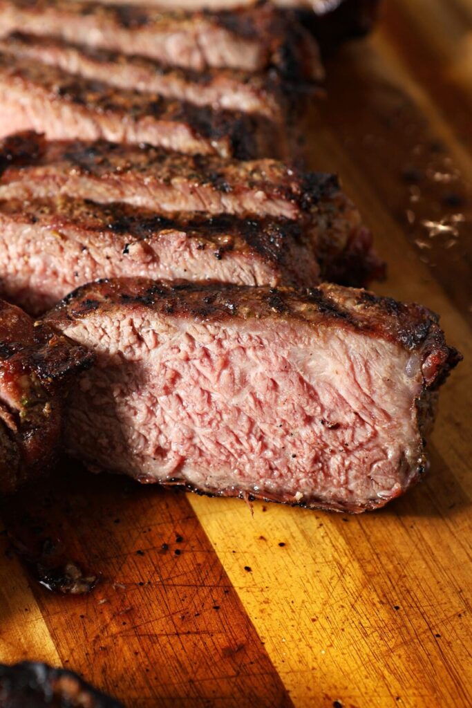 Sliced grilled steak on a golden brown cutting board