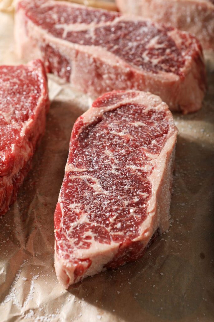 Close up of raw steaks seasoned with salt