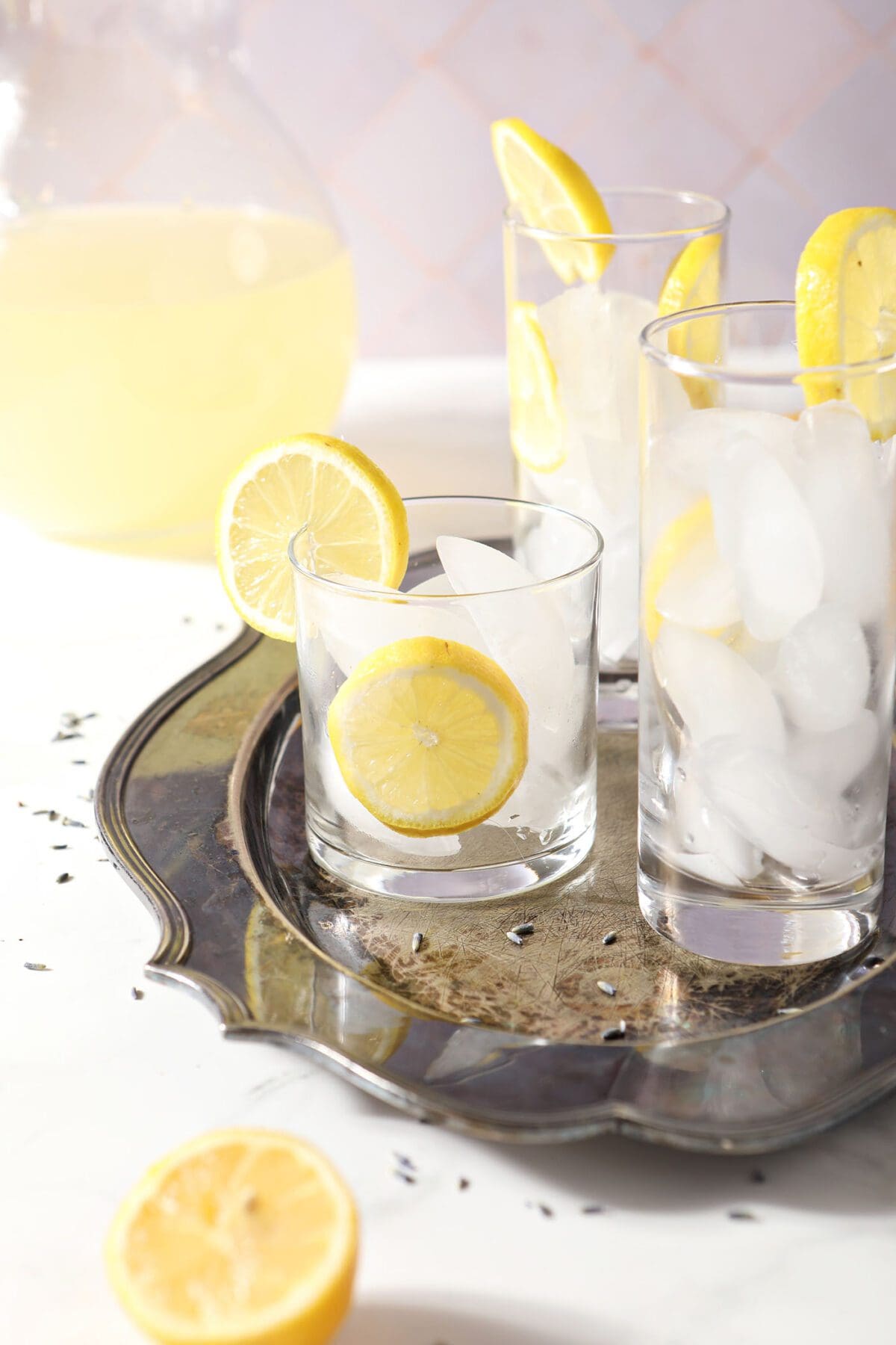 Three glasses filled with ice and lemon wheels sit on a silver platter