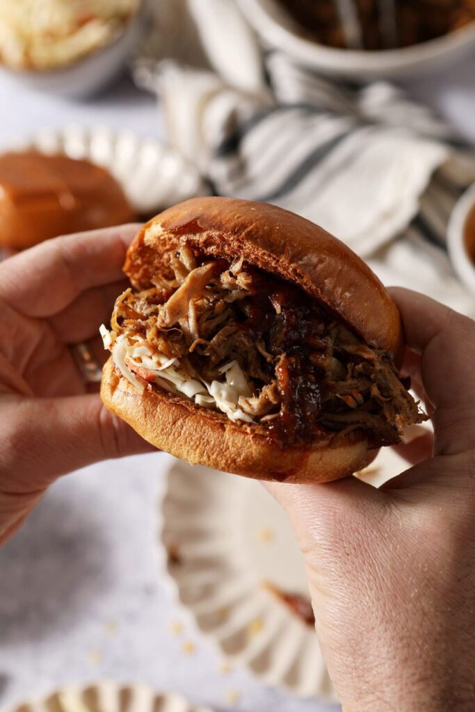 A man holds a BBQ sandwich over plates