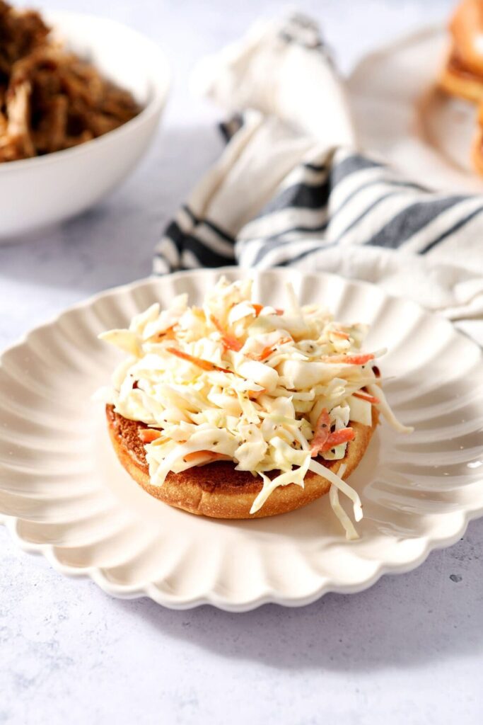 Homemade creamy coleslaw recipe on a bun on a white plate