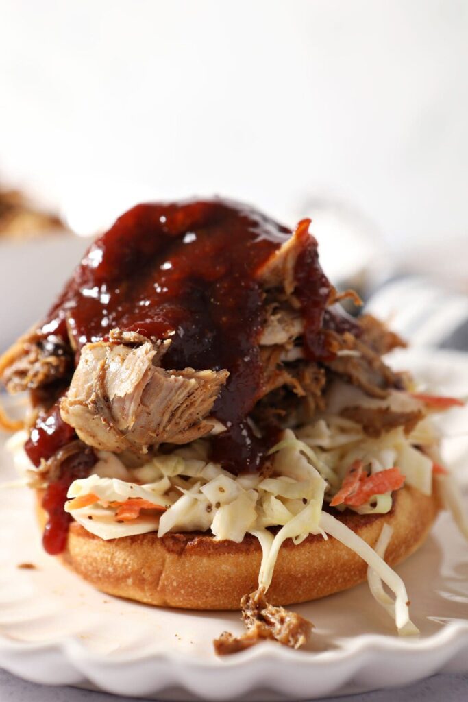 BBQ sauce on top of pulled pork and slaw on a bun