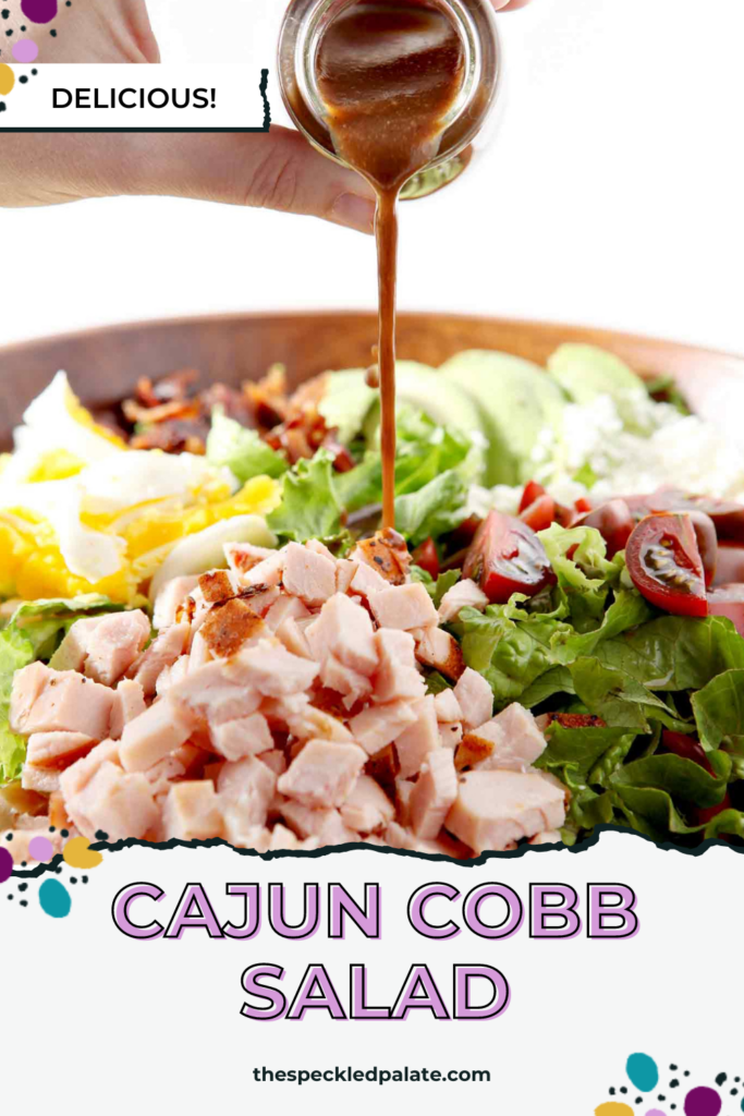 Dressing pours on top of a loaded salad in a bowl with the text Cajun Cobb Salad