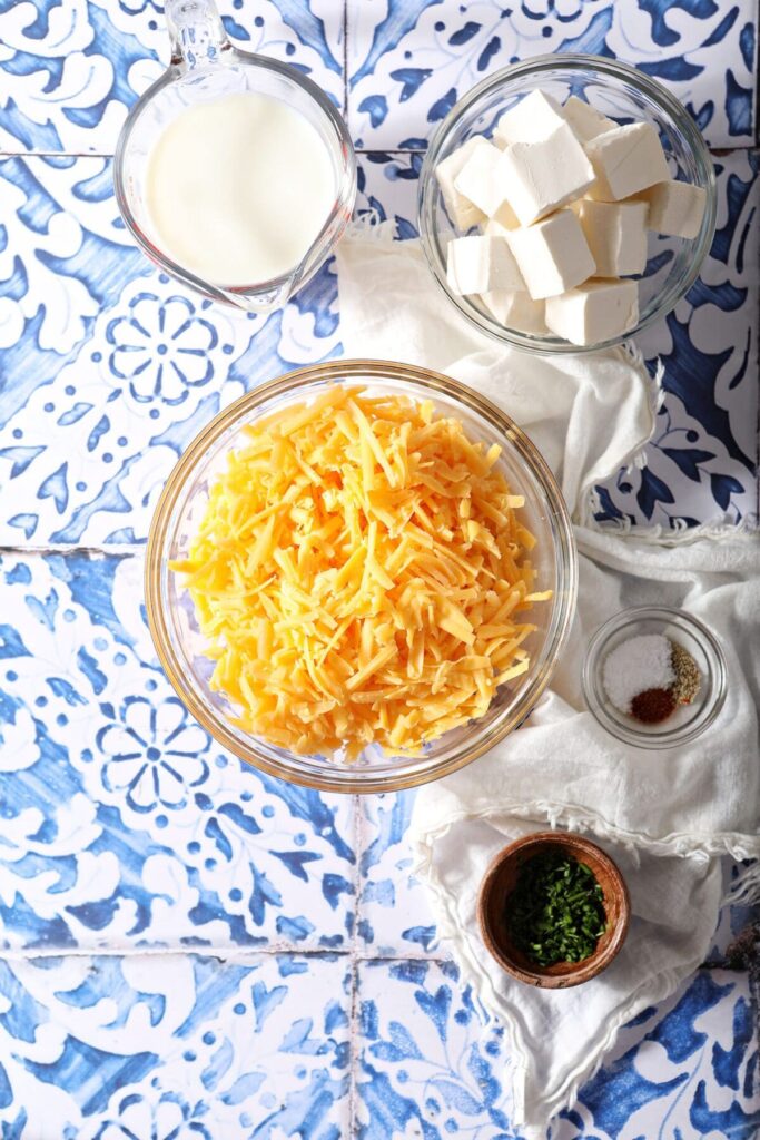 Ingredients to make cheese dip for pretzels in bowls on a blue patterned tile countertop