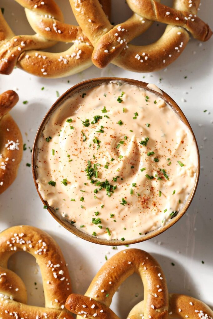 Close up of cheese dip garnished with paprika and chives and surrounded by soft pretzels