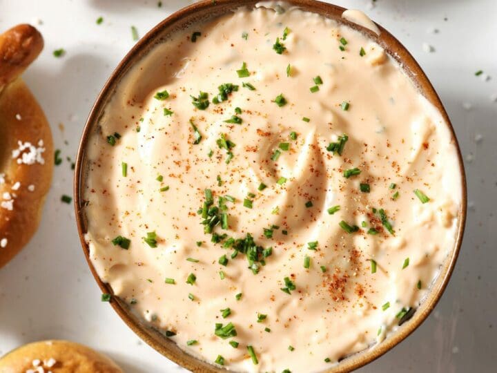 Close up of cheese dip garnished with paprika and chives and surrounded by soft pretzels