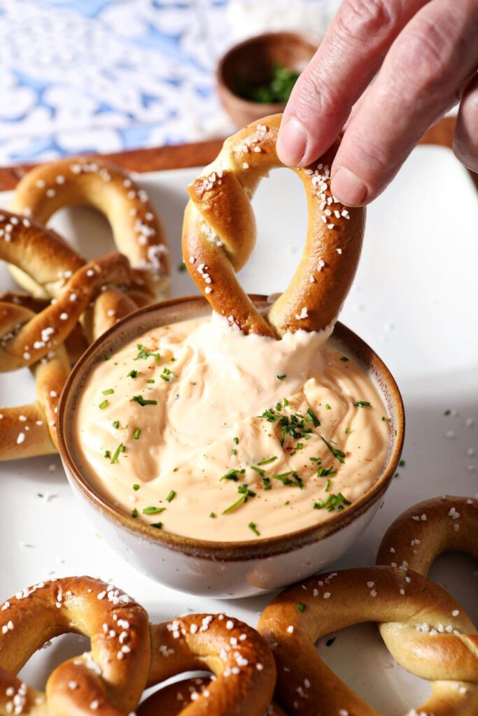 A soft pretzel dips into a bowl of cheese dip