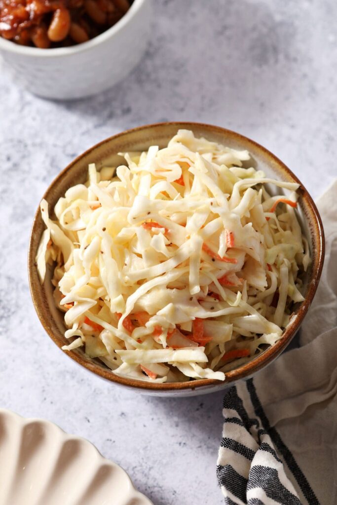 A bowl of coleslaw next to a bowl of baked beans