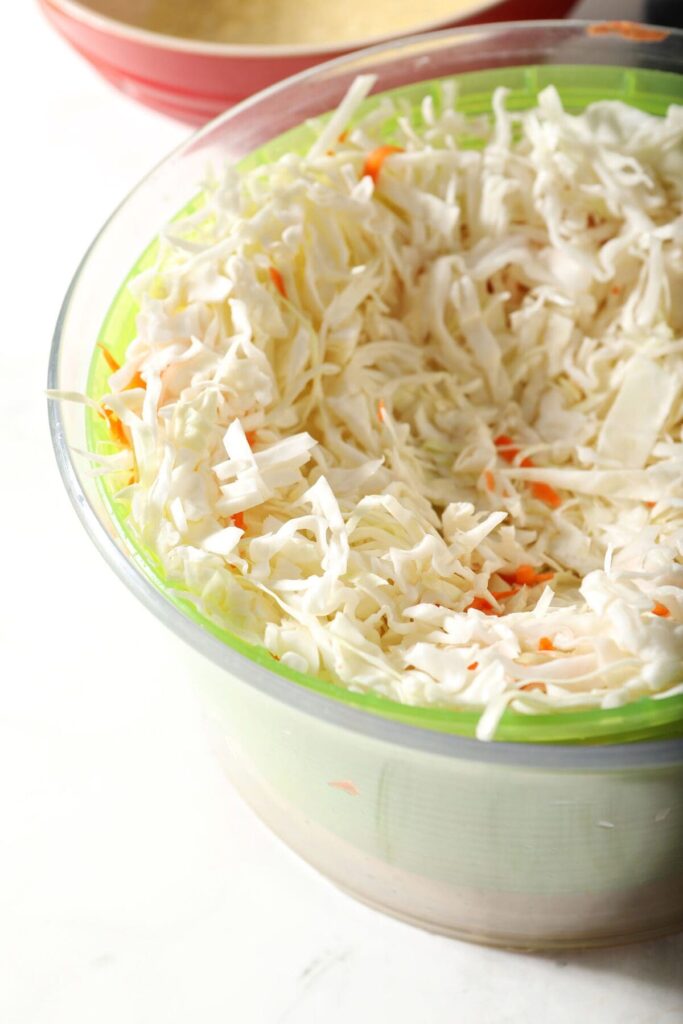 Cabbage and shredded carrots in a salad spinner on a marble surface