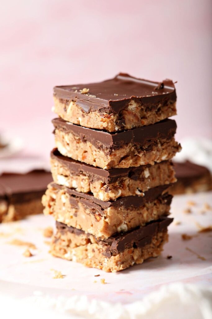 A stack of five chocolate covered peanut butter bars on parchment on a pink countertop