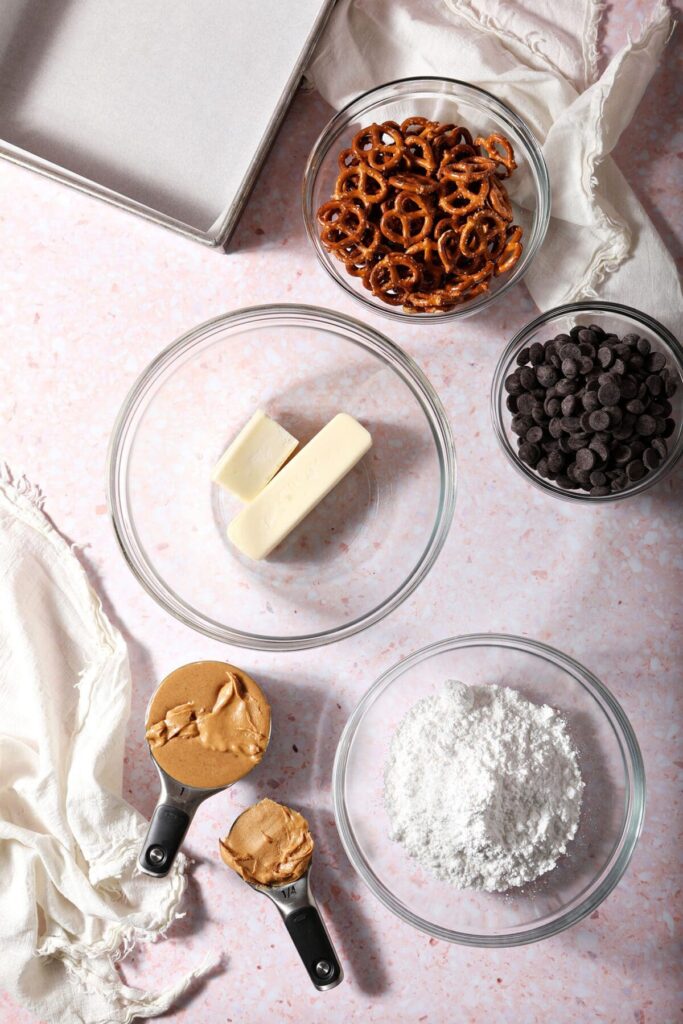 Ingredients to make no bake peanut butter bars in bowls on a pink countertop