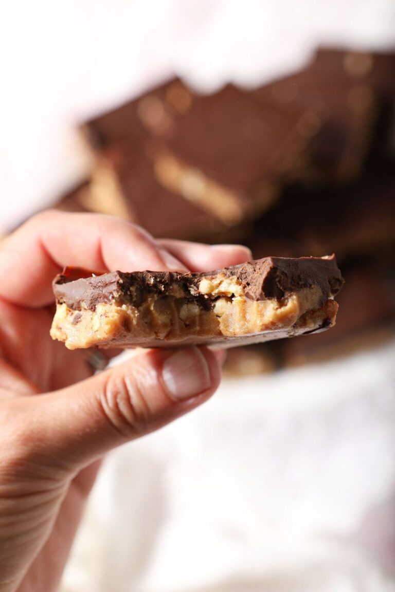 A hand holds a bitten-into Chocolate Peanut Butter Bar above a platter holding more