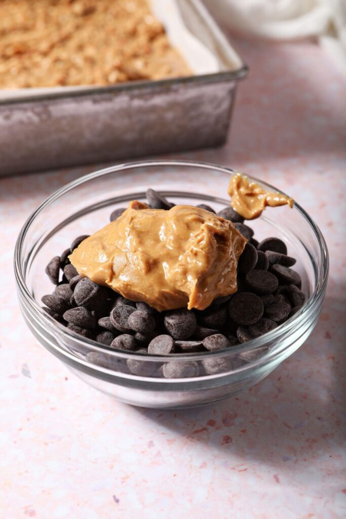 A dollop of peanut butter on top of chocolate chips in a clear glass bowl