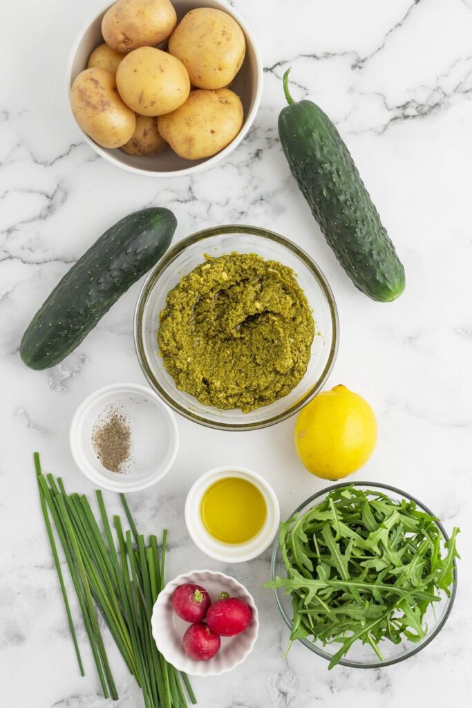 Ingredients to make roasted potato salad with pesto on marble in bowls