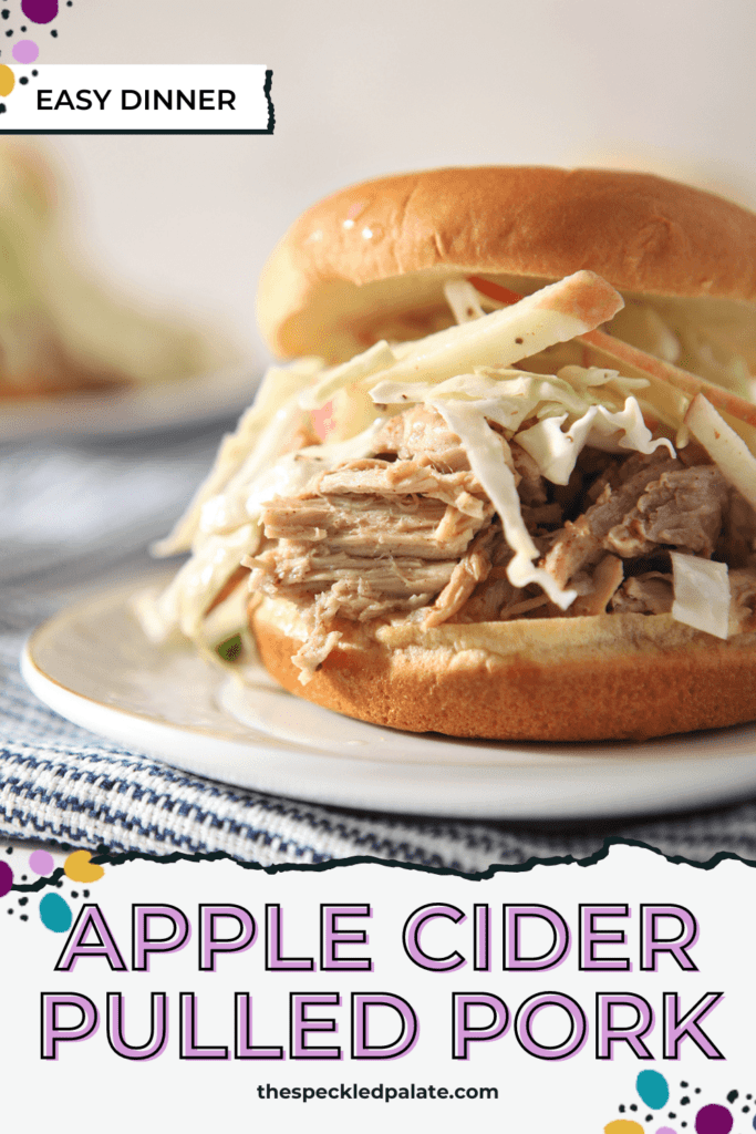 Close up of an Pulled Pork Sandwich with slaw on a white plate on top of a blue striped towel with the text Apple Cider Pulled Pork