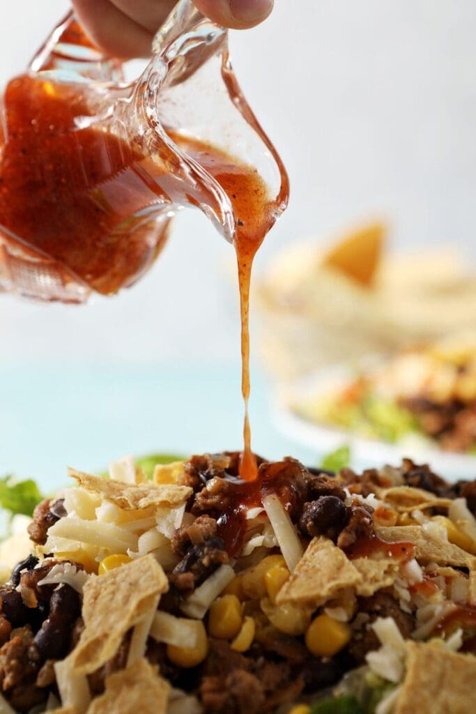 A glass vial of a red dressing pours on top of a taco salad