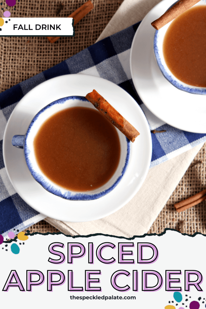 Overhead of two white mugs with blue rims full of apple cider on a tablescape with the text Spiced Apple Cider