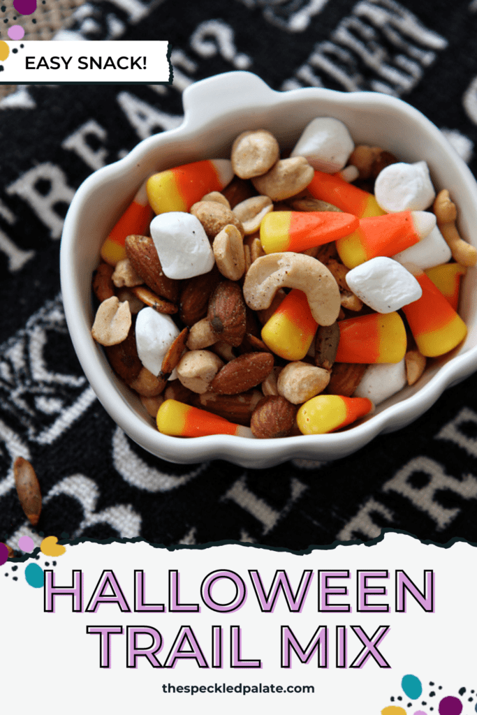 Close up of a pumpkin-shaped bowl holding a mixture of nuts, marshmallows and candy corn with the text Halloween Trail mix