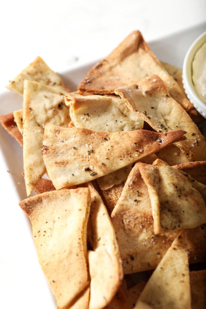 Crispy pita chips on a white plate next to a bowl of hummus