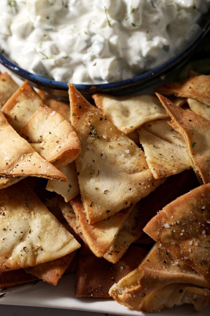 Close up of baked pita chips next to a bowl of homemade tzatziki sauce