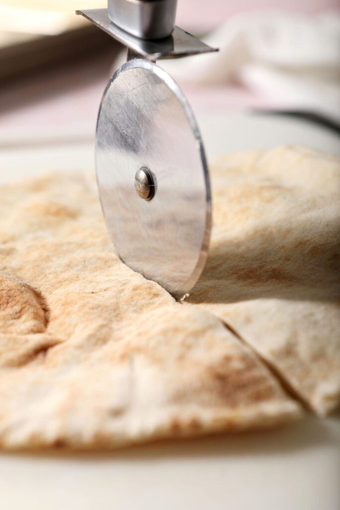 A pizza cutter slices a pita in half