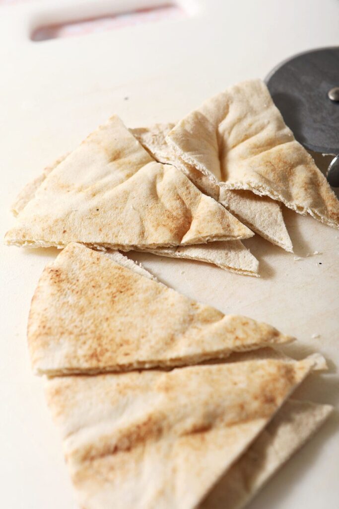 Pita triangles on a white cutting board next to a pizza cutter