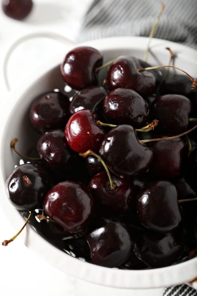 A white colander holds fresh cherries