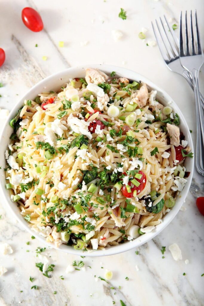 A bowl of lemon orzo pasta with chicken and veggies from above on a marble surface