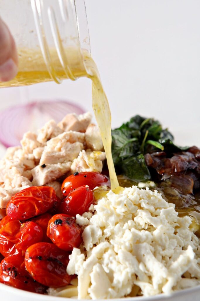 Lemon vinaigrette pours on top of ingredients in a white bowl to make orzo pasta salad