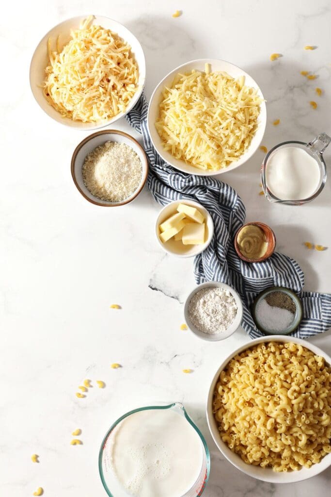 Ingredients to make three cheese stovetop macaroni and cheese on a marble surface in bowls