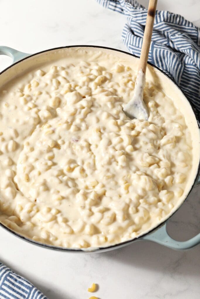 A saucepan full of stovetop macaroni and cheese with a wooden spoon inside it on marble