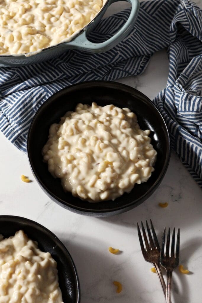 Two black bowls hold a serving of Three Cheese Mac and Cheese next to patterned blue napkins