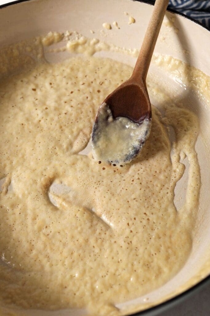 A golden brown roux in a pan with a wooden spoon