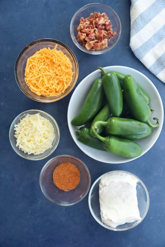 Ingredients to make jalapeño poppers on a blue countertop with a blue and white striped towel