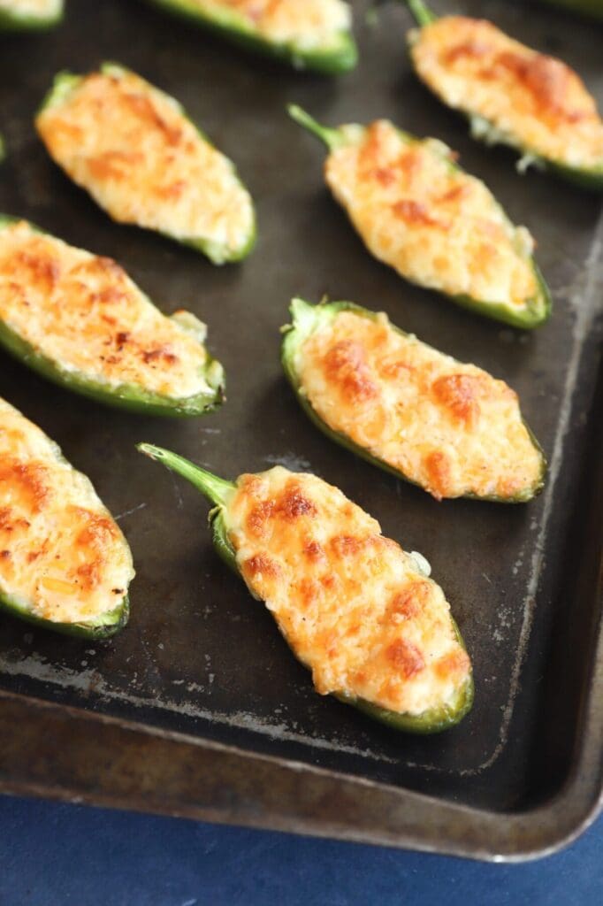 Golden brown baked jalapeño poppers on a black baking sheet after baking