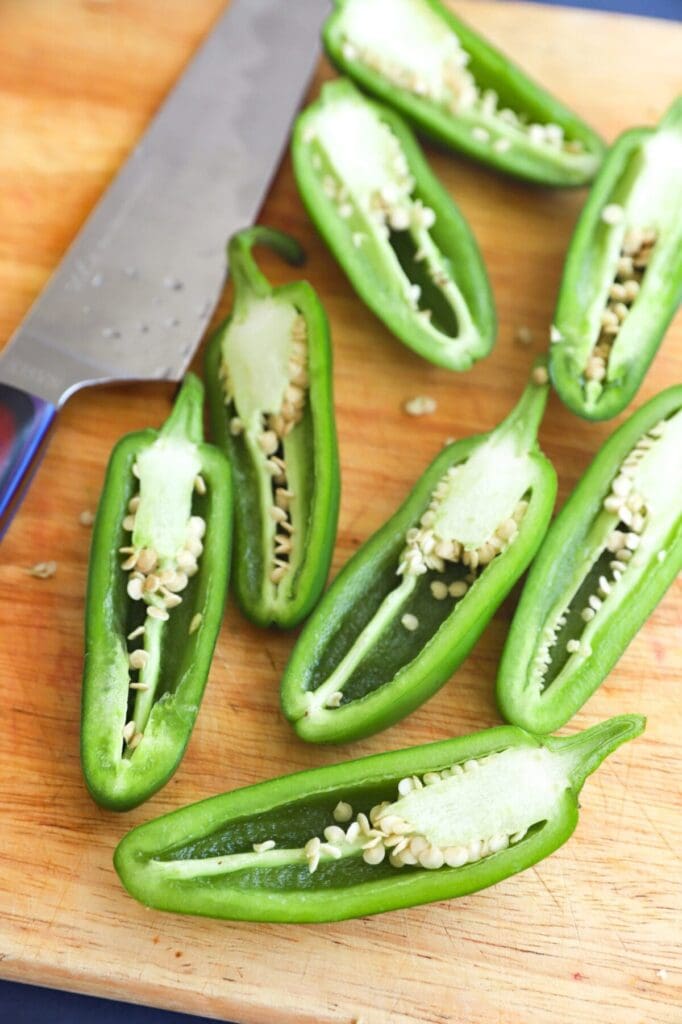 Halved jalapeños on a wooden cutting board with a knife