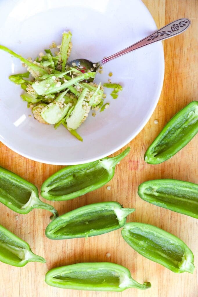 Seeded jalapeños with the membranes and seeds in a white bowl on a cutting board