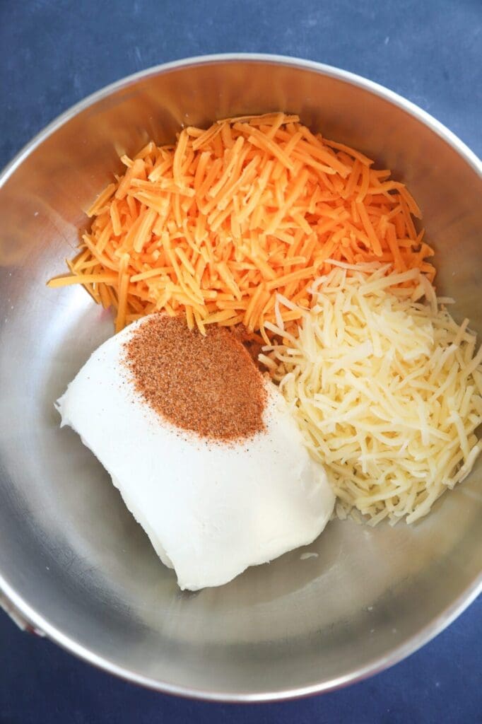 Cream cheese with shredded cheeses and spices in a mixing bowl