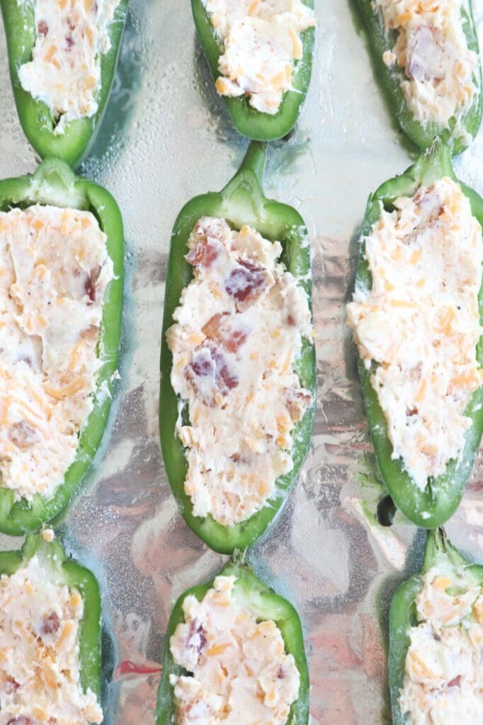 Halved jalapeños filled with cream cheese filling and bacon before baking