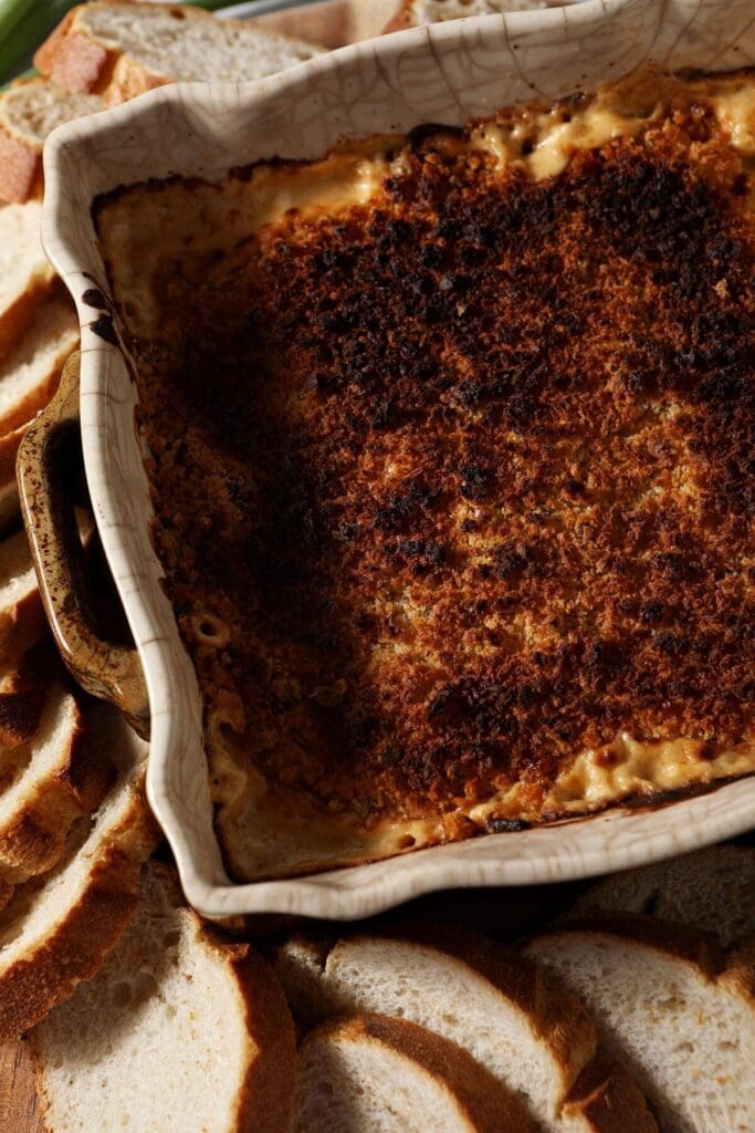 Baked crawfish dip in a casserole dish surrounded by sliced baguette