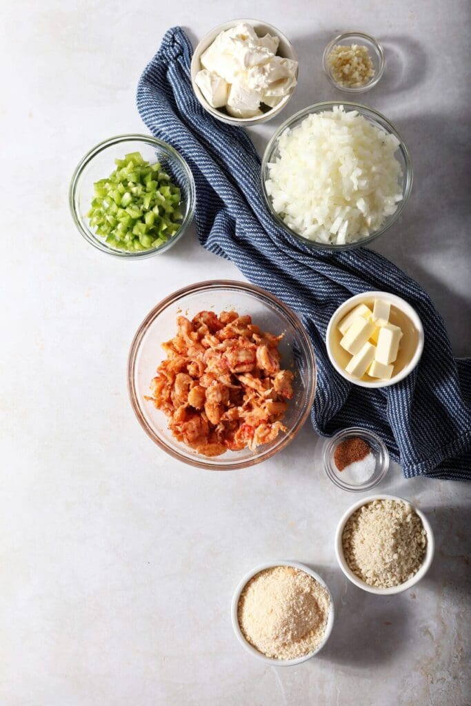 Ingredients to make crawfish dip in bowls on a gray surface with a dark blue towel