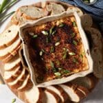Hot crawfish dip in a casserole dish surrounded by baguette slices and garnished with green onion