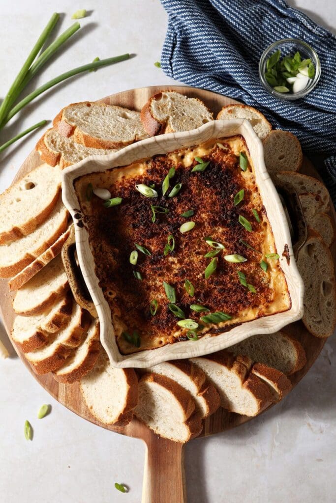 Hot crawfish dip in a casserole dish surrounded by baguette slices and garnished with green onion