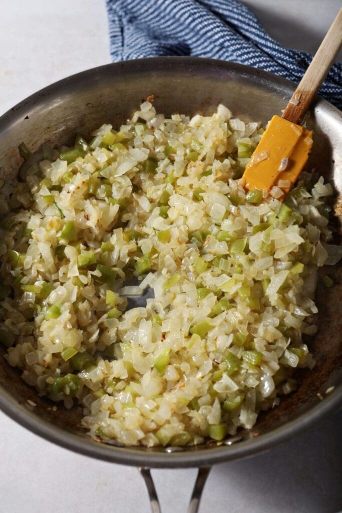 Cooked down onions, green bell pepper and garlic in a pan with a yellow rubber spatula