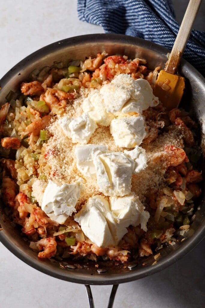 Cream cheese and parmesan on top of crawfish and other ingredients in a skillet