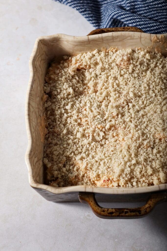 Crawfish dip topped with panic breadcrumbs in a casserole dish before baking