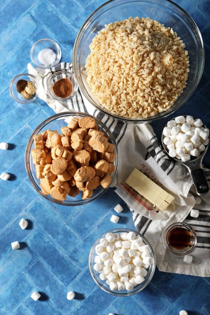 Bowls of ingredients to make Rice Krispie treats with pumpkin spice flavors on a blue tile surface