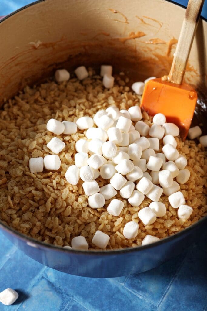 Rice Krispie cereal and mini marshmallows on top of melted marshmallows to make Pumpkin Spice Rice Krispie Treats