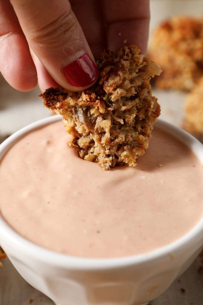 A hand dips a boudin ball into an orangish dipping sauce